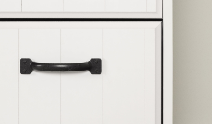 A matte finish black metal handle on a white kitchen drawer door.