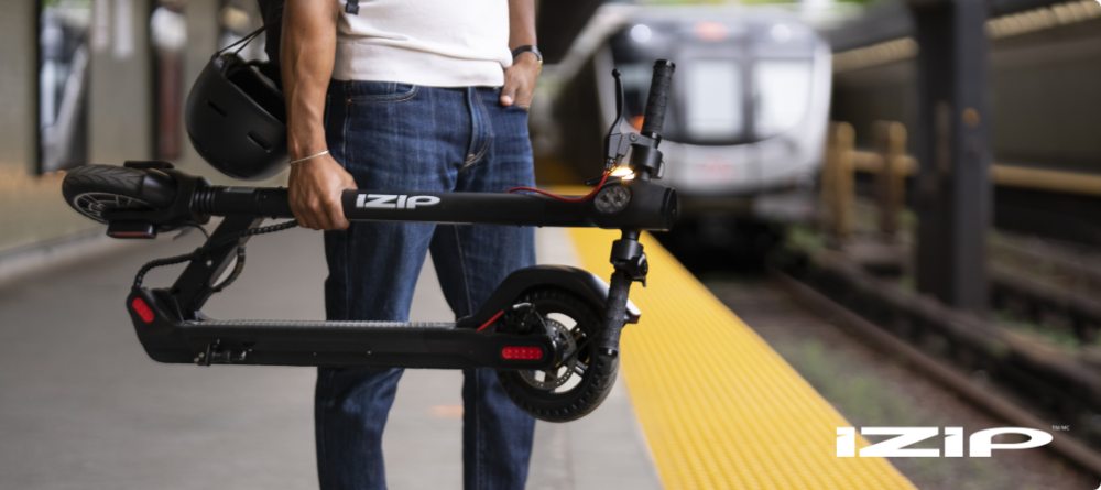 Person holding a folded-up iZip e-scooter on a subway platform.