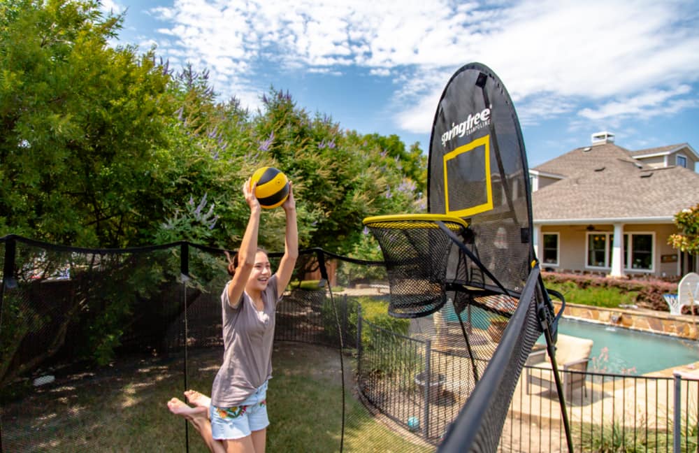 Une jeune fille lançant une balle dans un filet alors qu’elle saute sur une trampoline.