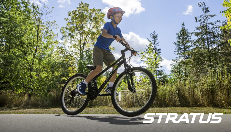 A child rides a Stratus bike along a tree-lined street.