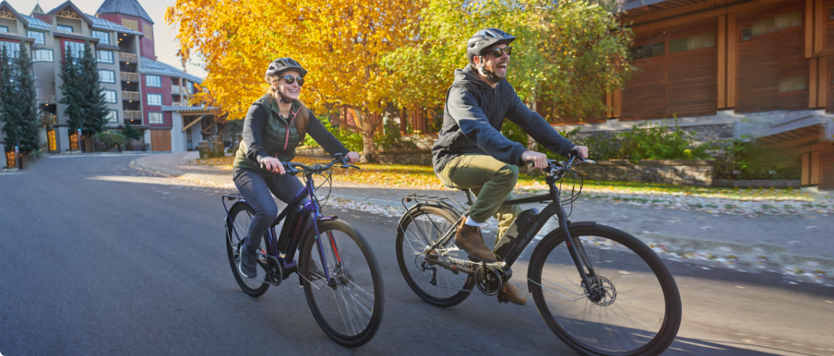 Deux personnes font du vélo Raleigh dans une rue résidentielle ensoleillée.