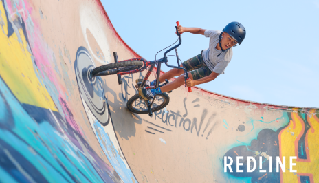 A young person rides a Redline BMX bike on a dirt ramp.