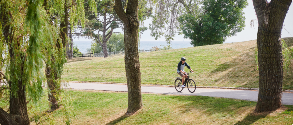 Un homme fait du vélo Raleigh dans une rue urbaine bordée d'arbres.