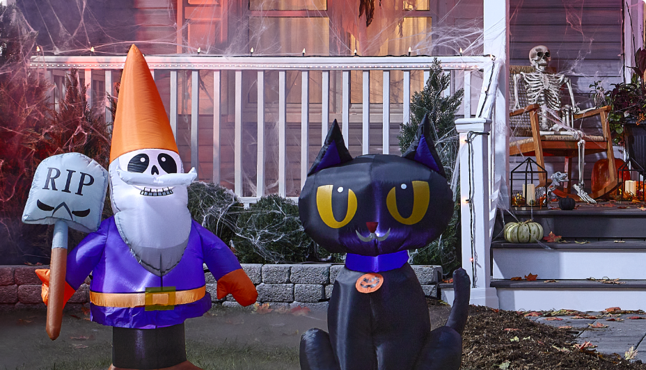 Front porch decorated with a standing witch, glowing skeleton, tombstones and ghost stakelights on Halloween night