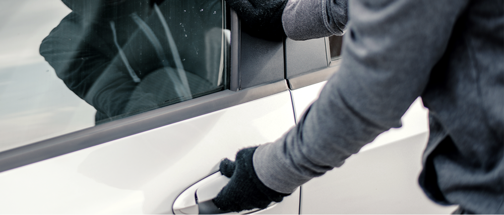 A figure wearing gloves tries the handle of a parked car.