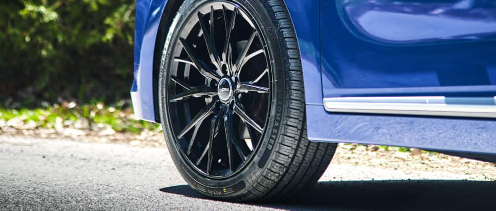 Gros plan sur un pneu MotoMaster Hydra Edge Tour monté sur une voiture bleue.