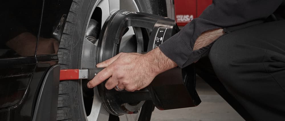 A mechanic applies an alignment tool to the front tire of a black car.