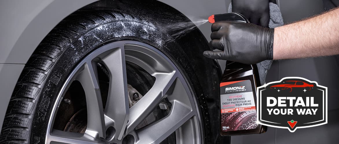 A hand in a nitrile glove sprays SIMONIZ Graphene Tire Dressing onto the side wall of a tire.