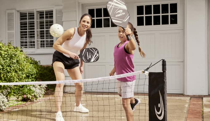 A woman and a child playing pickleball in a driveway.