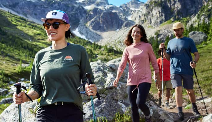 A family dressed in Woods apparel hiking outdoors with walking sticks. 