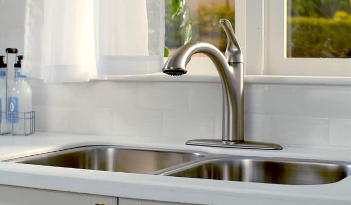 Closeup shot of a brushed-nickel finish faucet by a kitchen sink.