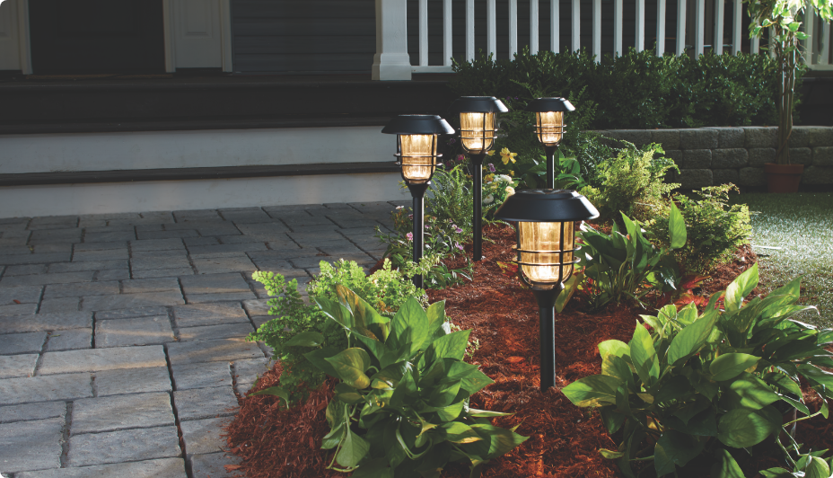 Four NOMA Outdoor Warm White LED Solar Garden & Pathway stake lights in a garden.