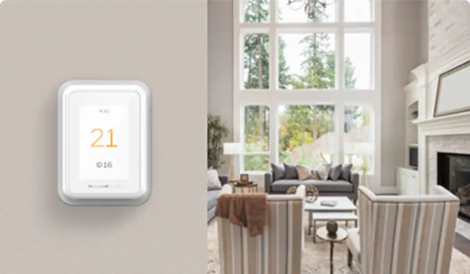 Smart thermostat on a wall displaying the temperature as 21 degrees Celsius indoors and 16 degrees outdoors.