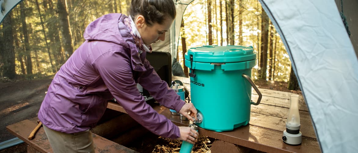 Woman filling water bottle from a Woods bucket cooler at campsite