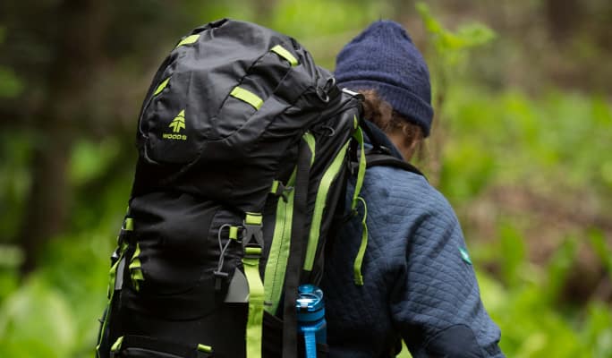 A WOODS backpack strapped to an adult hiker’s back. 