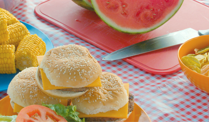 Burgers, corn and watermelon on a picnic table  