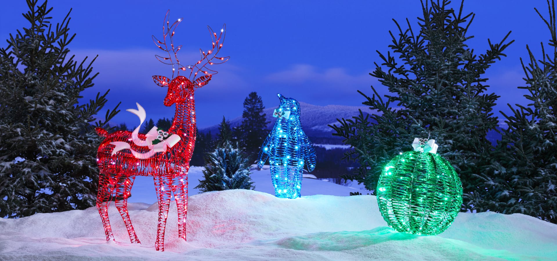 An assortment of pre-lit wireform figures on a snowy lawn including a reindeer, bear and ornament