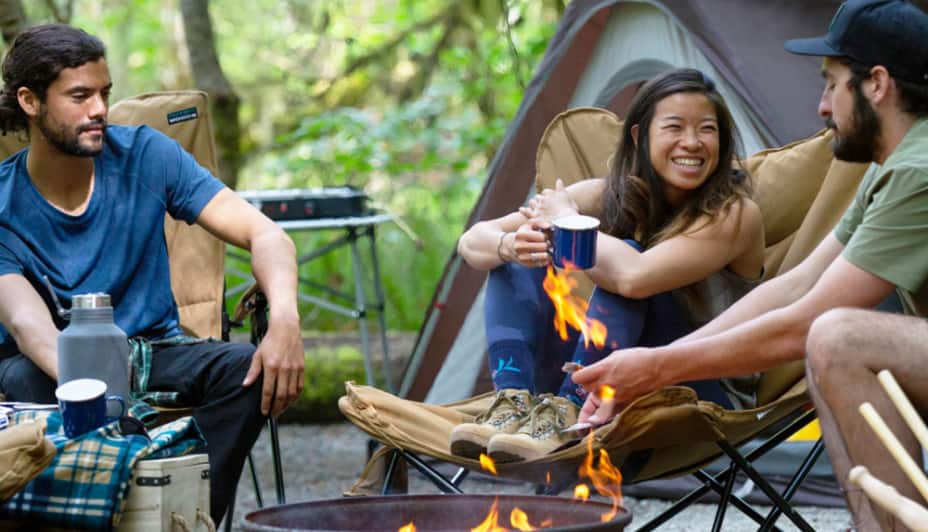 Deux hommes et une femme contemplant un feu de camp à proximité d'une tente 