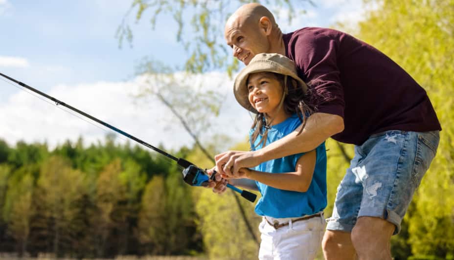 Father and daughter reeling in a fishing outdoors