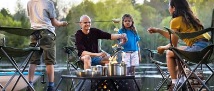 Father and two young kids make smores over a campfire