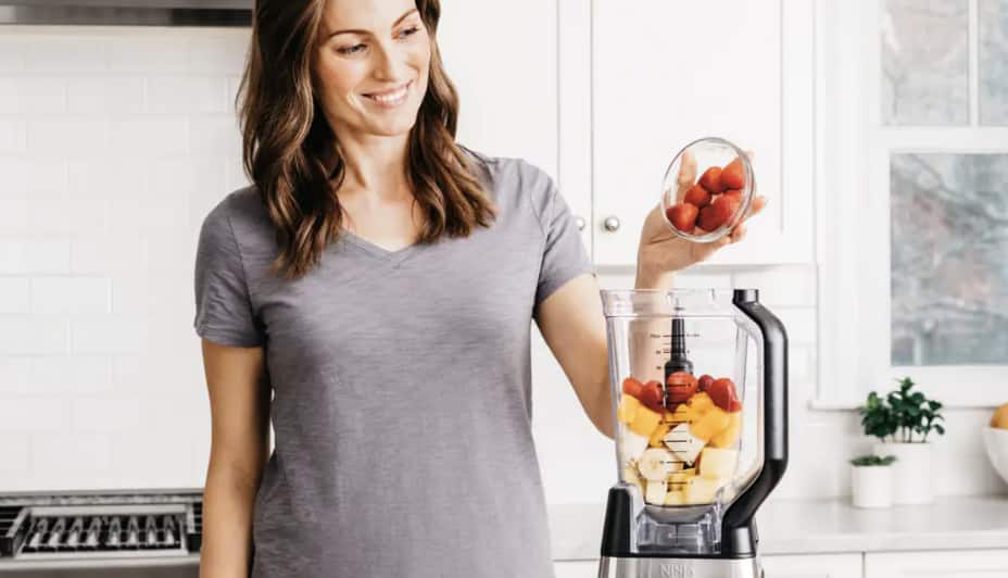 Une femme met des fruits dans un mélangeur
