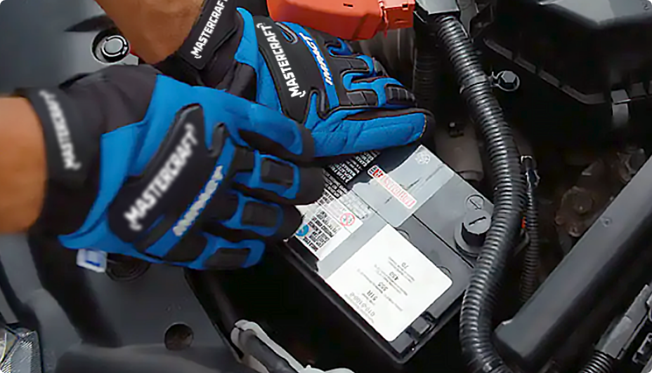 Une personne portant des gants installant une batterie de voiture 