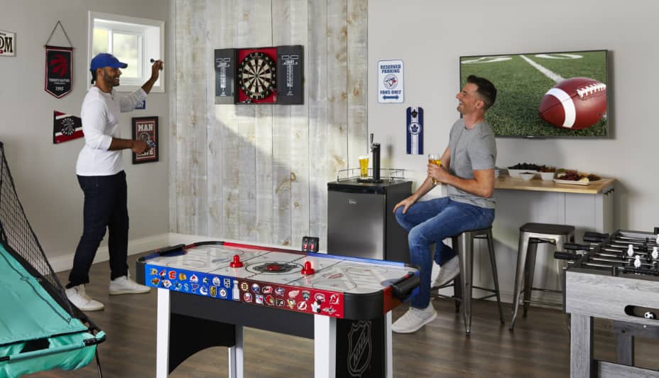 Two people in a rec room with a dartboard, air hockey table and foosball table