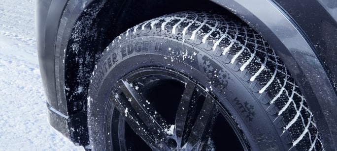 Un pneu MotoMaster Winter Edge II monté dans le passage de roue d'une voiture sur une route enneigée.