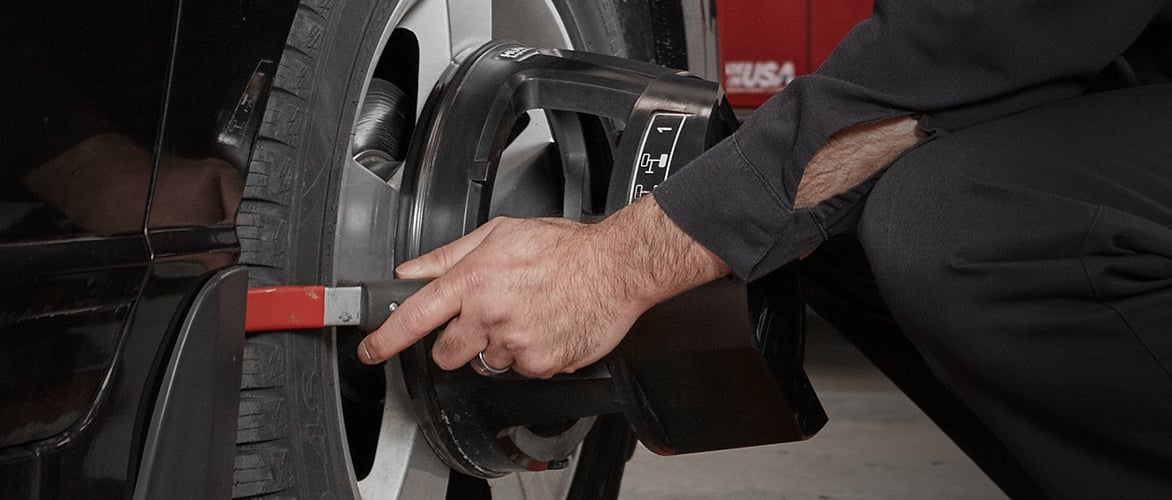Un mécanicien agenouillé règle la roue avant d'une voiture.