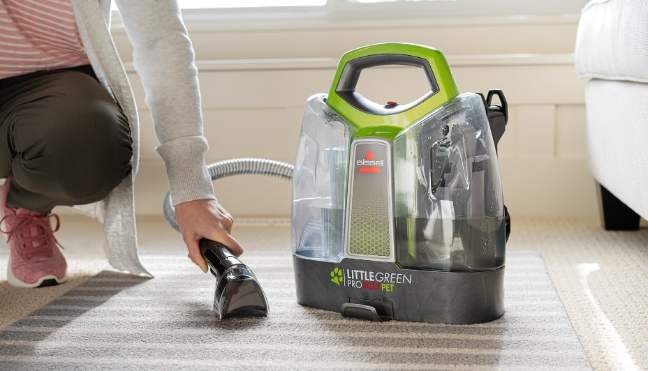 A person cleans a throw rug with a carpet cleaner.