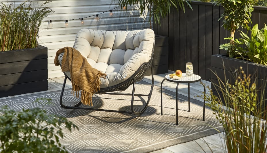 A cushioned CANVAS Cove Rocking Papasan Chair and side table on a patio. 
