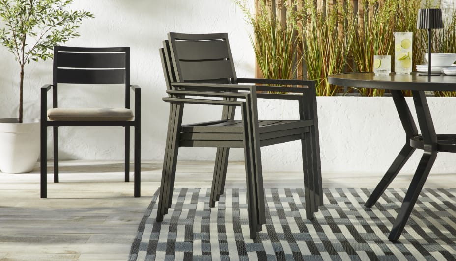 Three CANVAS Hastings Chairs stacked on a patio next to a dining table. 