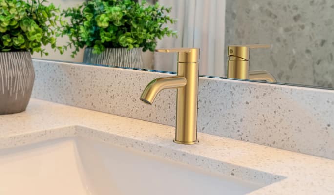 A gold Danze Crete Single Handle 4- in Centerset Bathroom Sink Faucet in a speckled-marble bathroom.