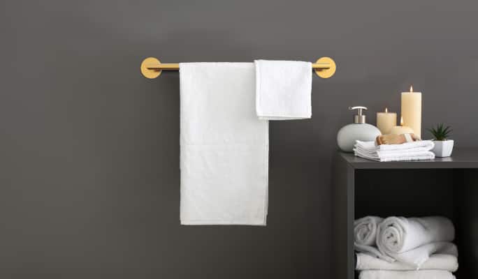 Un porte-serviettes Danze Crete doré portant deux serviettes blanches monté sur un mur de salle de bain gris foncé.