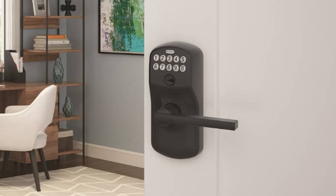 A matte black Schlage Latitude Plymouth Keypad Door Lever mounted on door of a home office.