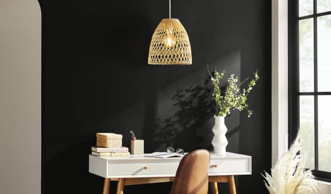 A gold chandelier hangs above a white desk in front of a black wall.