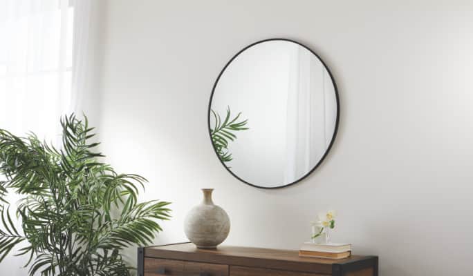 A circular mirror mounted on a grey wall above a wooden dresser.