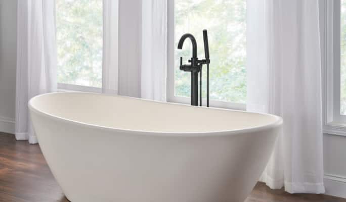 Un robinet noir mat de plancher Delta 1H avec douchette installée sur une baignoire blanche.