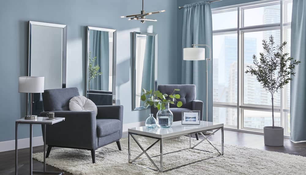 A stylish blue-grey living room with chrome furniture and design elements, a chandelier, mirrors and lamps.