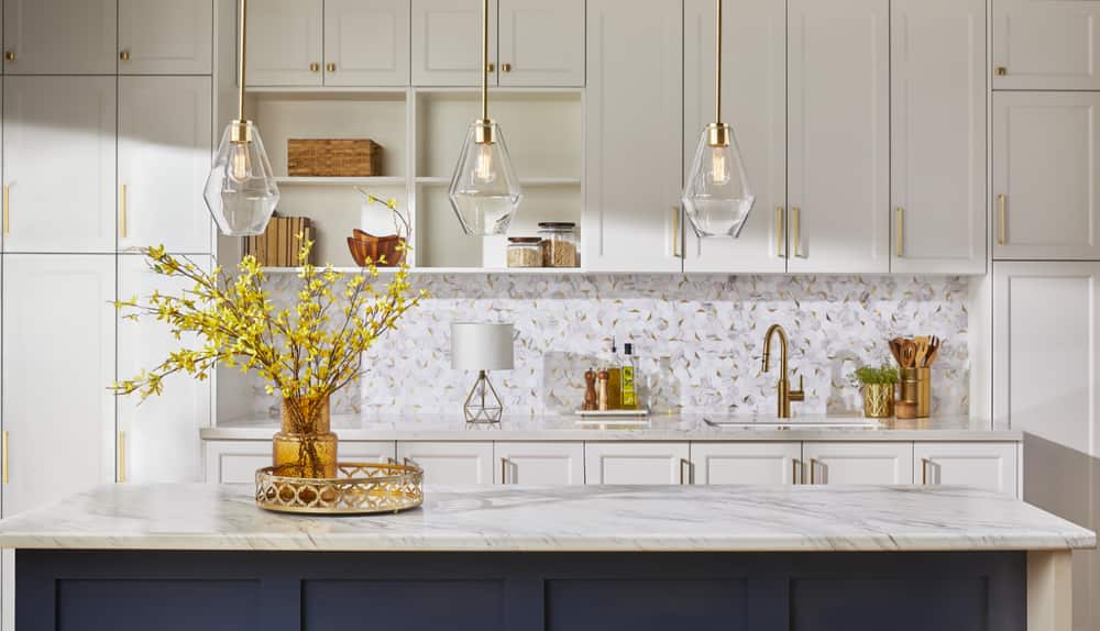 A bright kitchen with gold design elements, including pendant chandeliers, faucets and cupboard pulls.