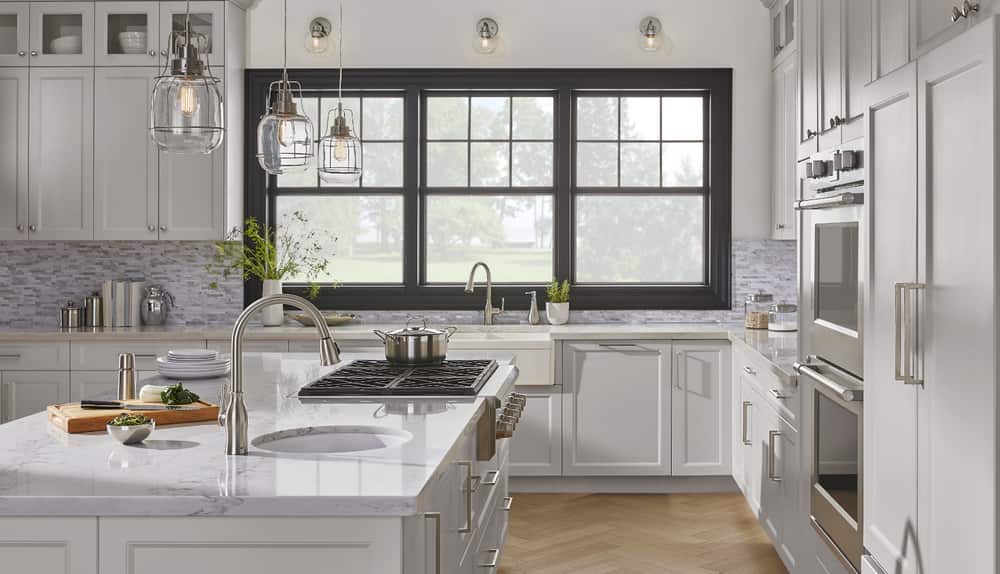 A bright kitchen with brushed nickel design elements, including pendant chandeliers, faucets and cabinet pulls.