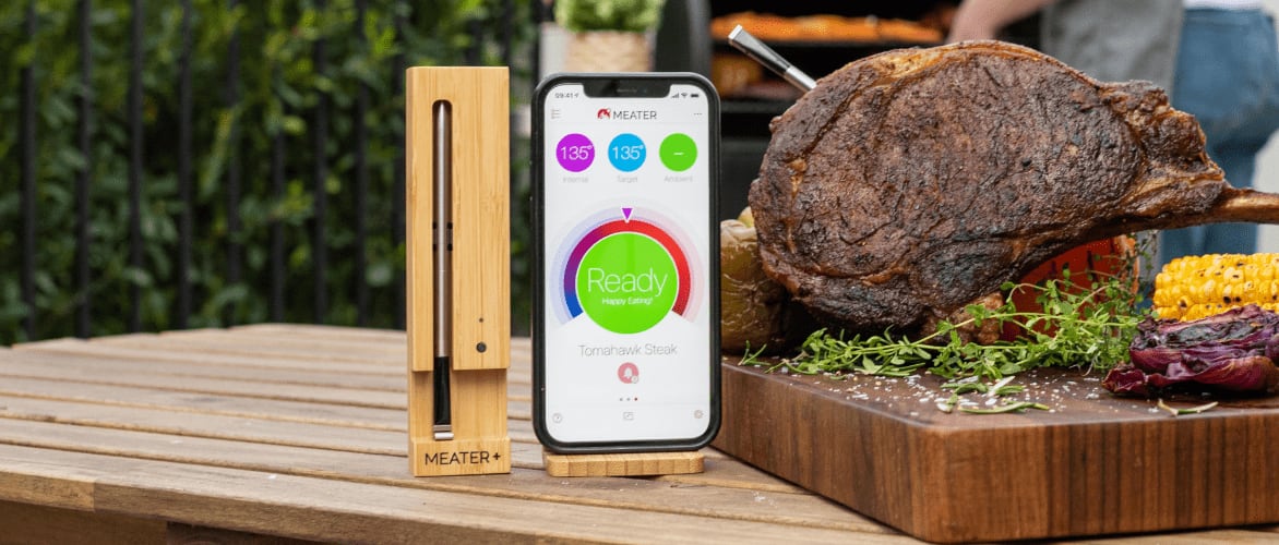 Un thermomètre intelligent sans fil MEATER et une application sur un téléphone intelligent à côté d’un rôti cuit.
