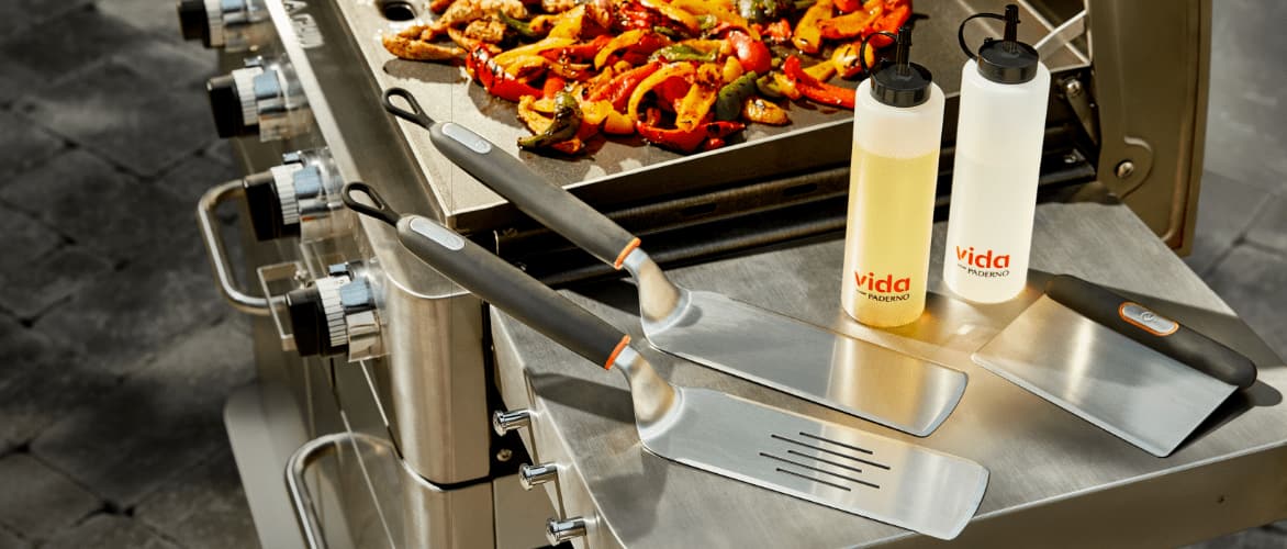 A set of Vida by PADERNO griddle spatulas, scraper and squeeze bottles on the side of a griddle. 