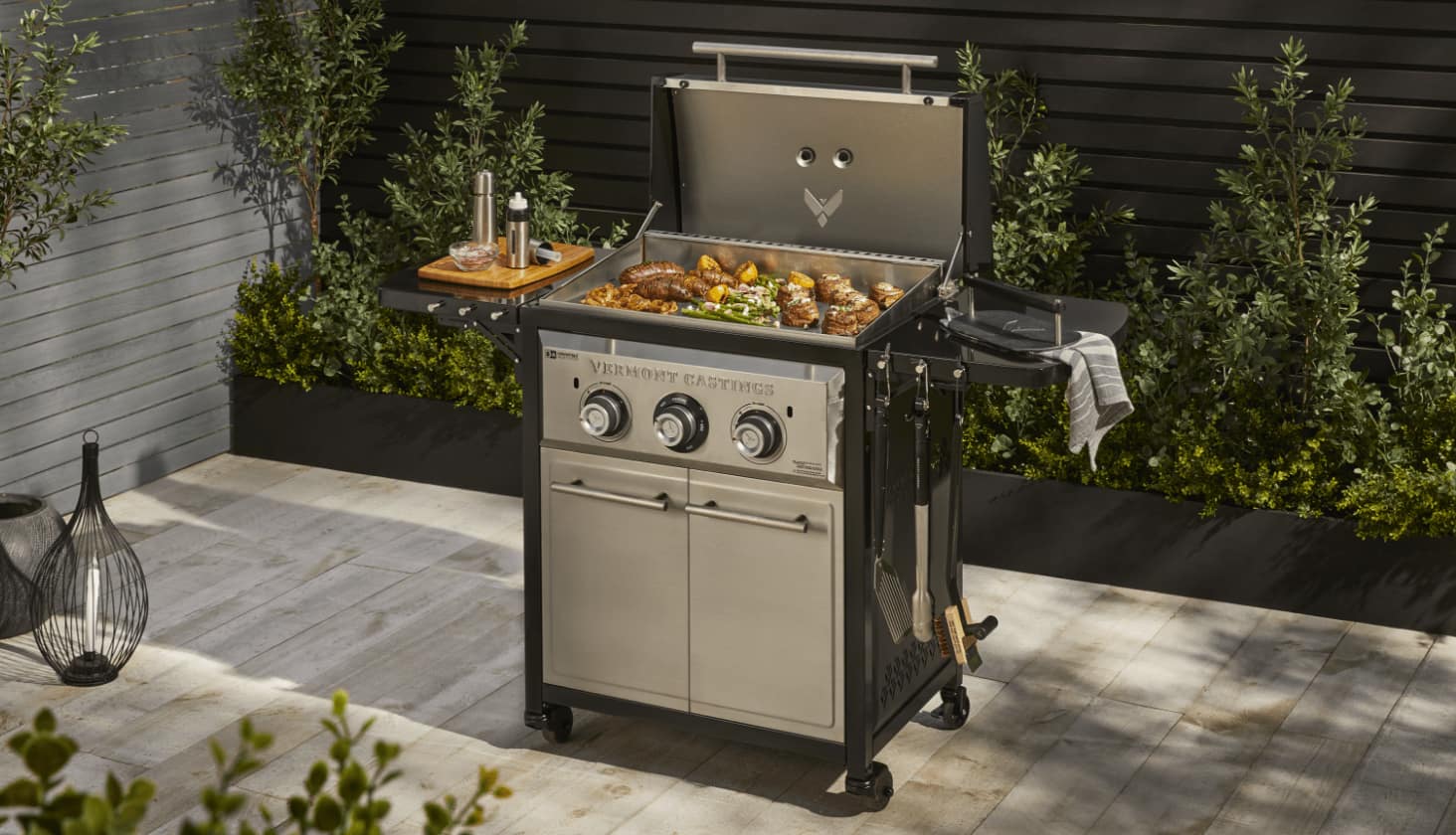Various foods cooking on a Vermont Castings 2-Burner Griddle on a patio. 