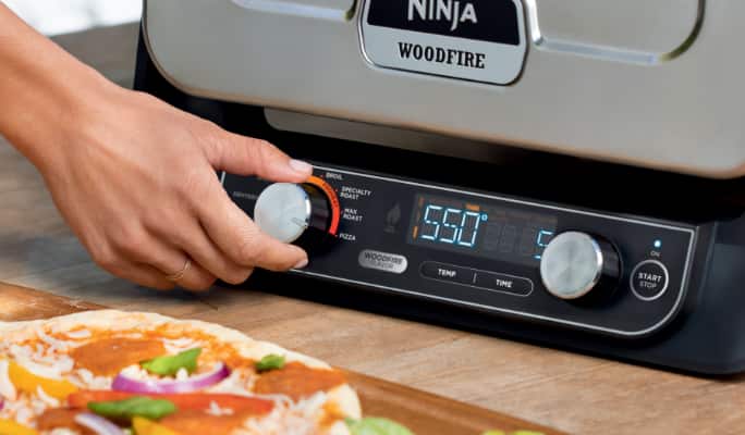  A person setting a temperature with a dial on a Ninja Woodfire Outdoor Oven.