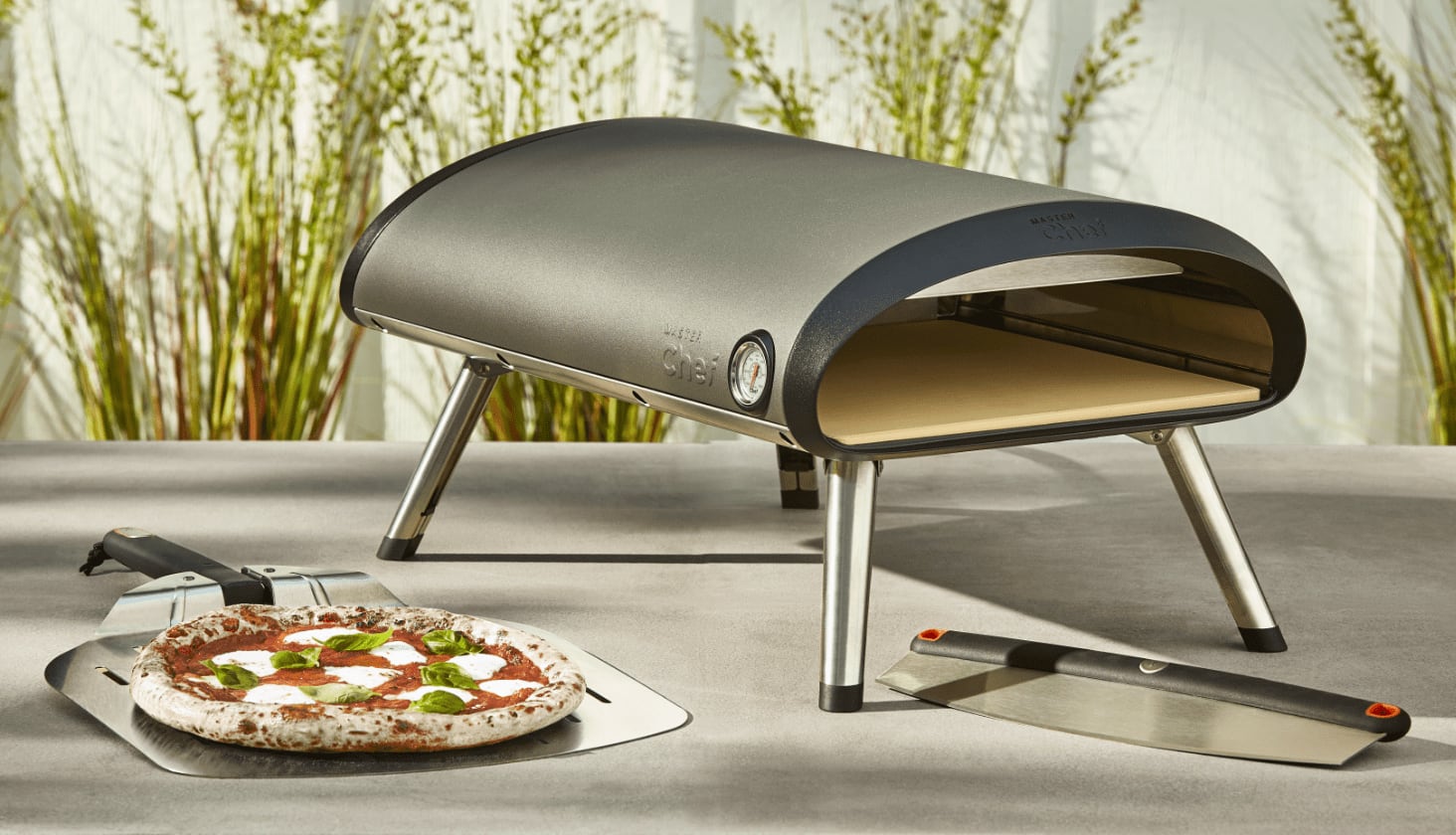 A MASTER Chef Gas Pizza Oven on an outdoor table with a cooked pizza. 