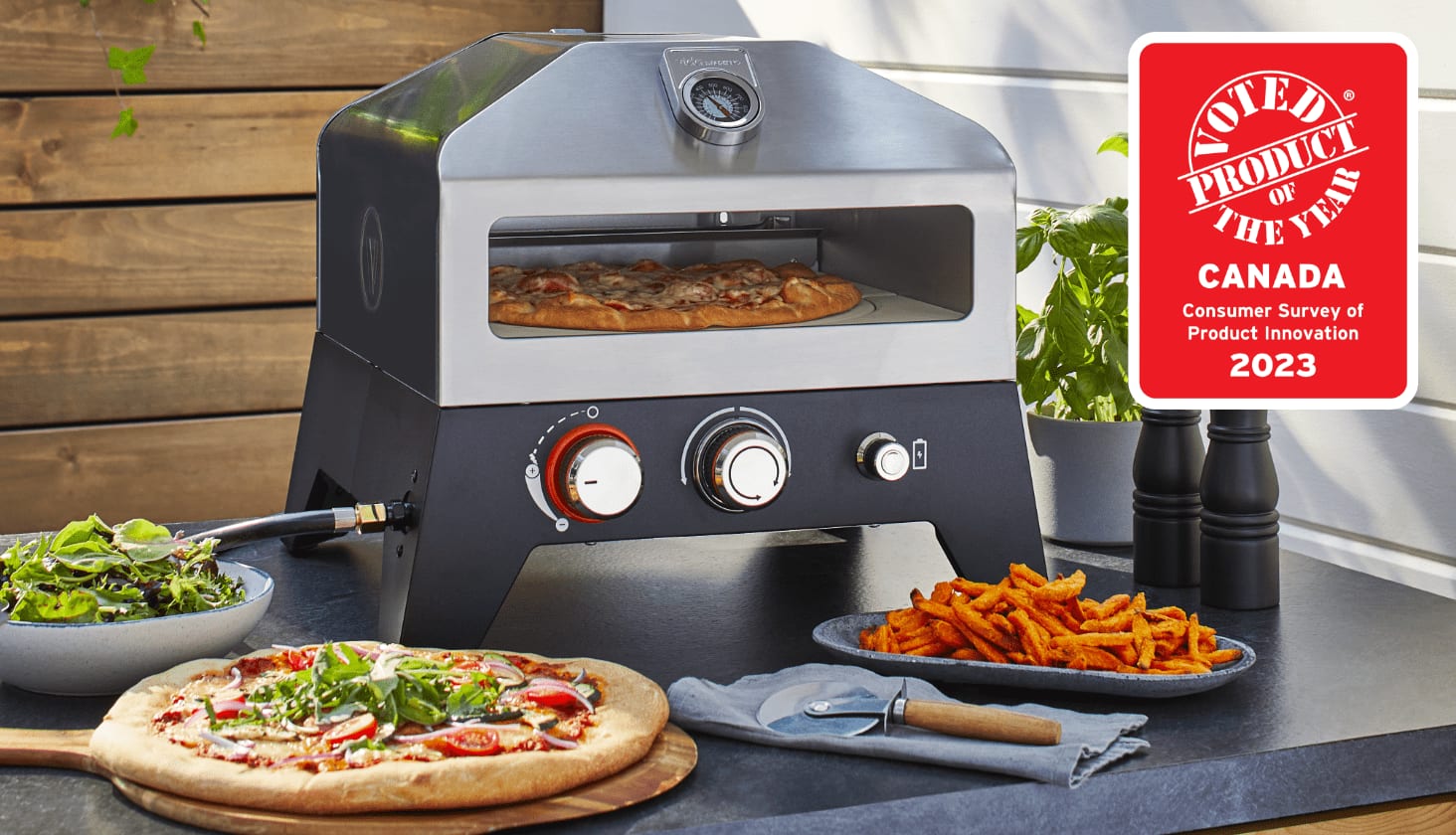 A Vida by PADERNO Gas Pizza Oven on an outdoor table with a cooked pizza and French fries. 