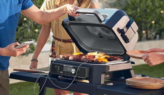 A person checking burgers cooking on a Ninja Woodfire Pro Connect XL Grill & Smoker.