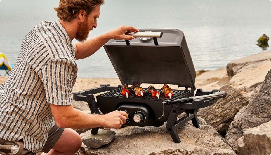 A man on a rocky beach grilling food on a Vermont Castings Portable BBQ.