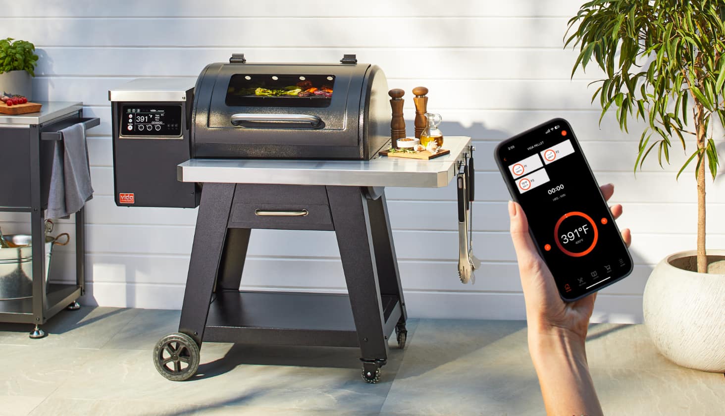 An adult checking the temperature of a VIDA by PADERNO Pellet Smart Grill on a smartphone.